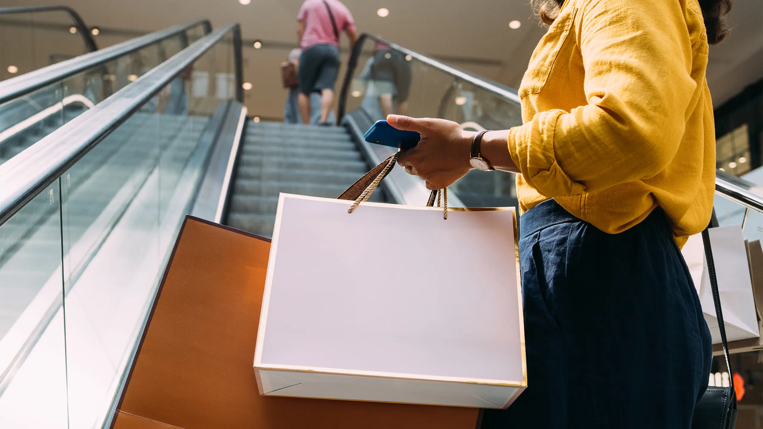 A woman holding paper bags and her mobile phone while going shopping