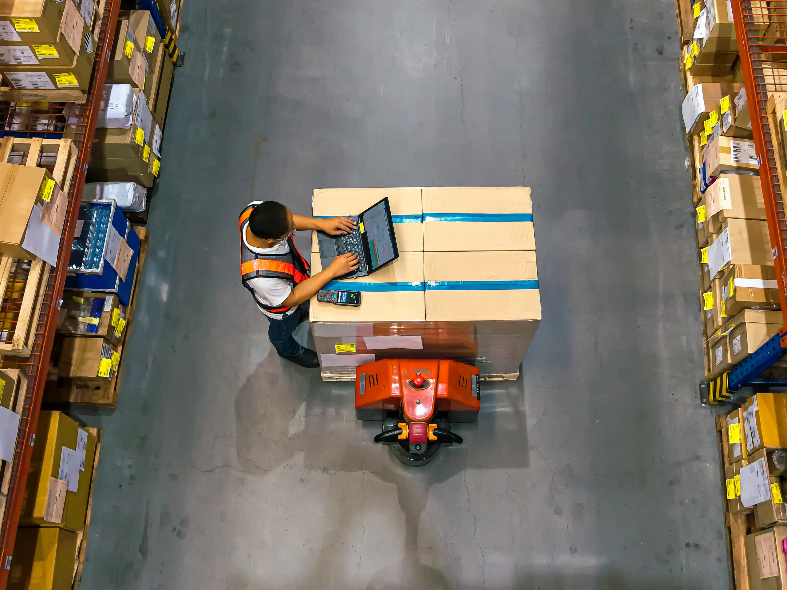 Top-view of a warehouse worker using a laptop to check the location of goods