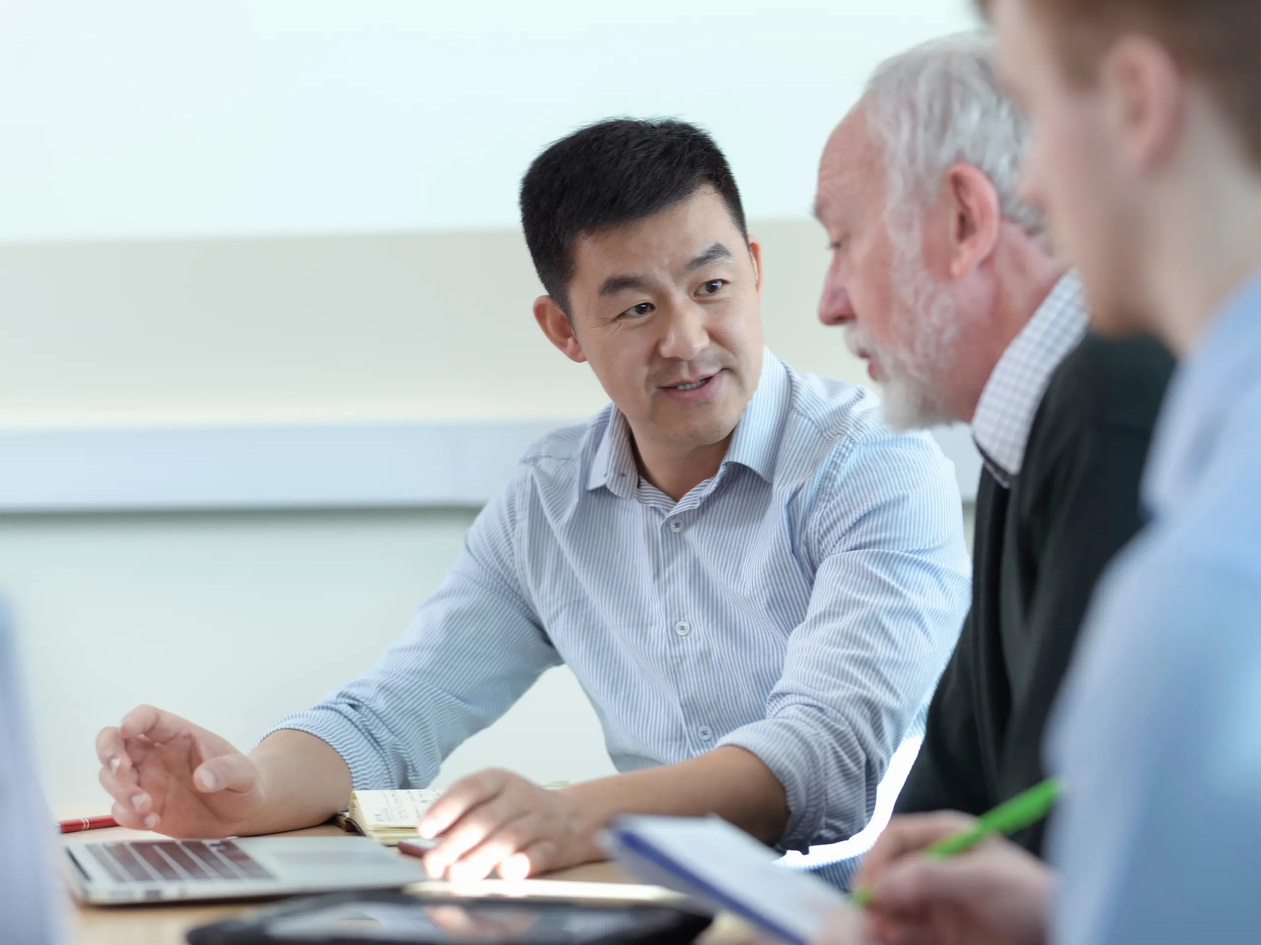 Younger and older colleagues discuss a project in a meeting room Younger and older colleagues discuss a project in a meeting room