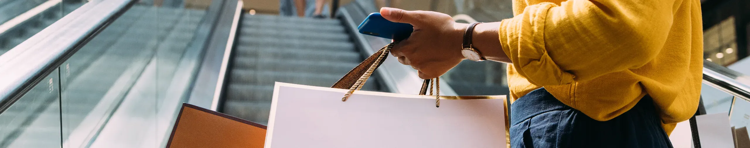 A woman holding paper bags and her mobile phone while going shopping